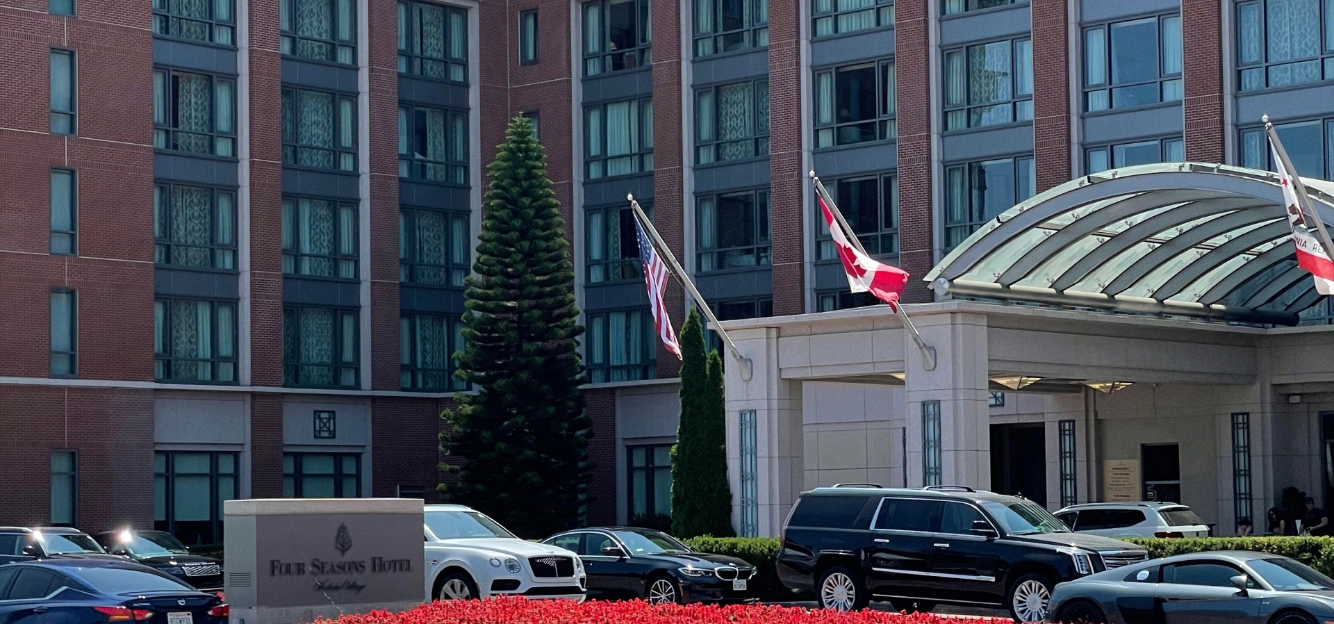 Hotel entrance with flags and parked cars.